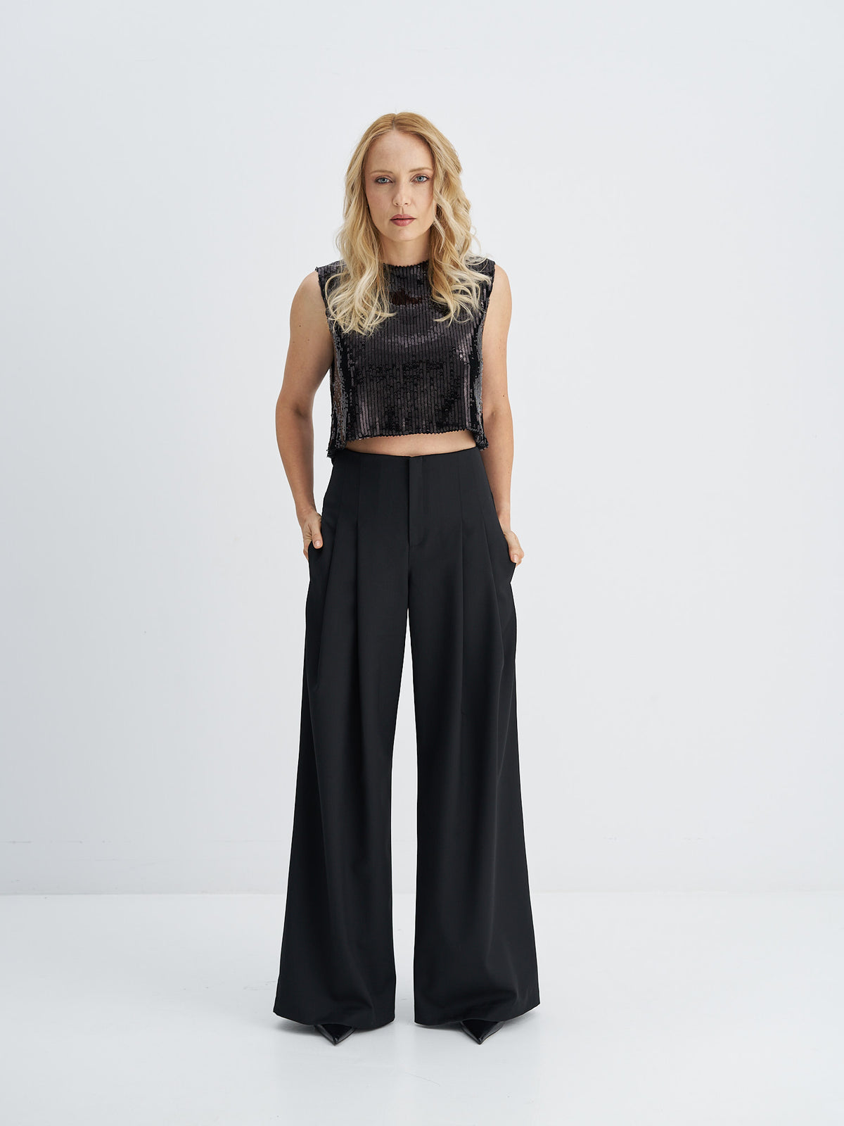 Black sleeveless sequin crop top worn with high-waisted wide-leg black trousers