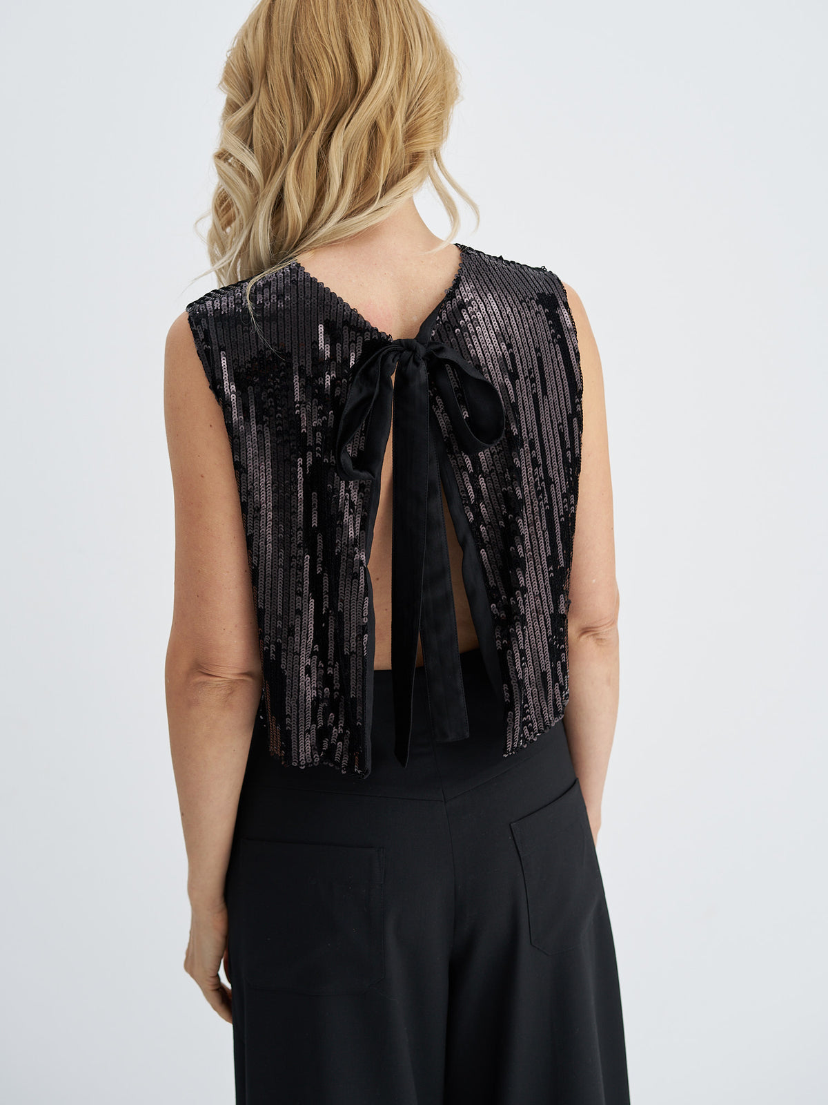 Close-up of black sequin top showing the bow fastening and open back