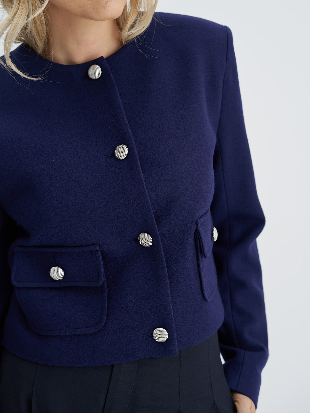 Close-up of indigo navy wool jacket showing textured silver buttons and buttoned patch pockets