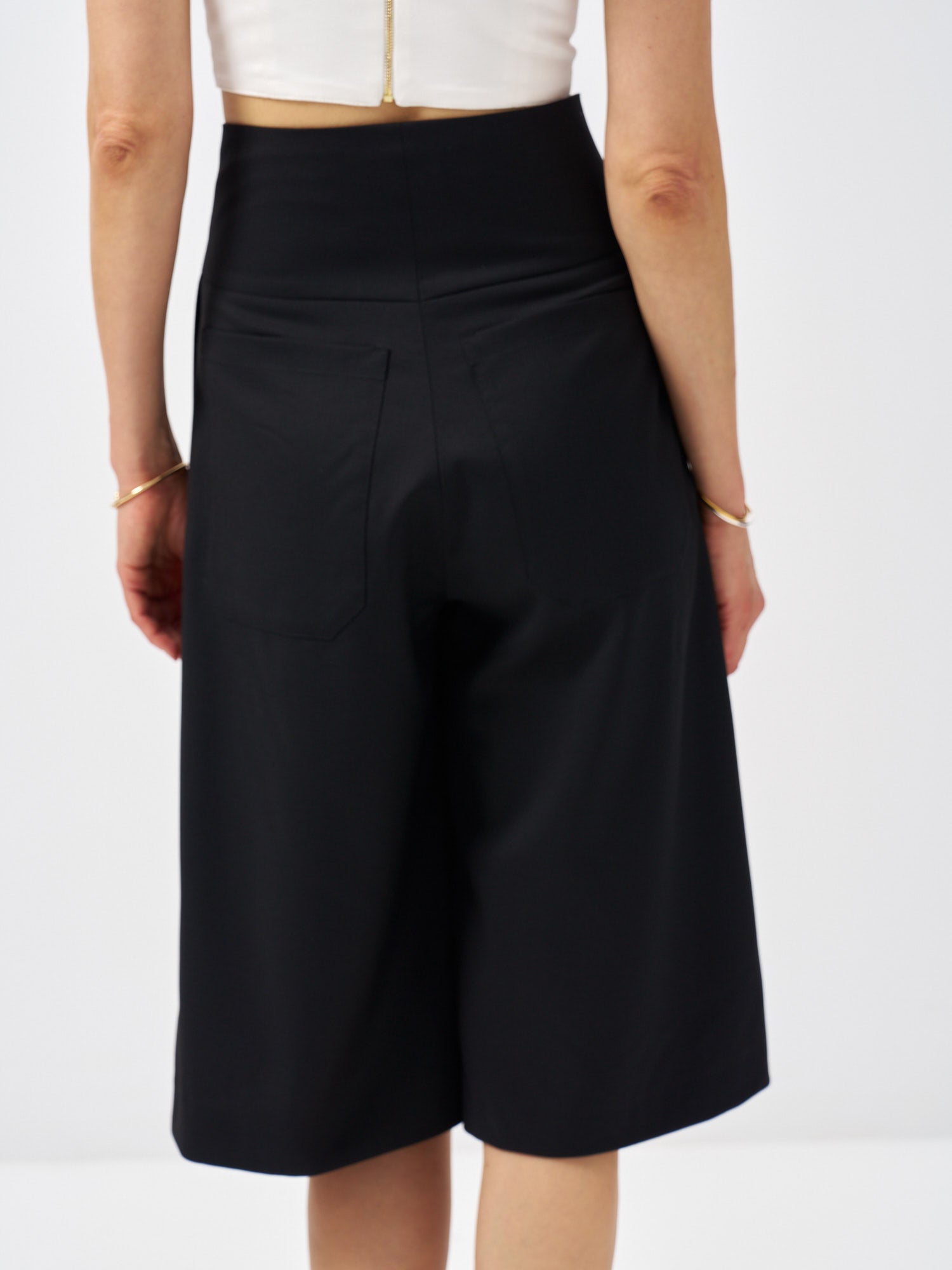 Back view of black wool bermuda shorts with patch pockets and a tailored fit