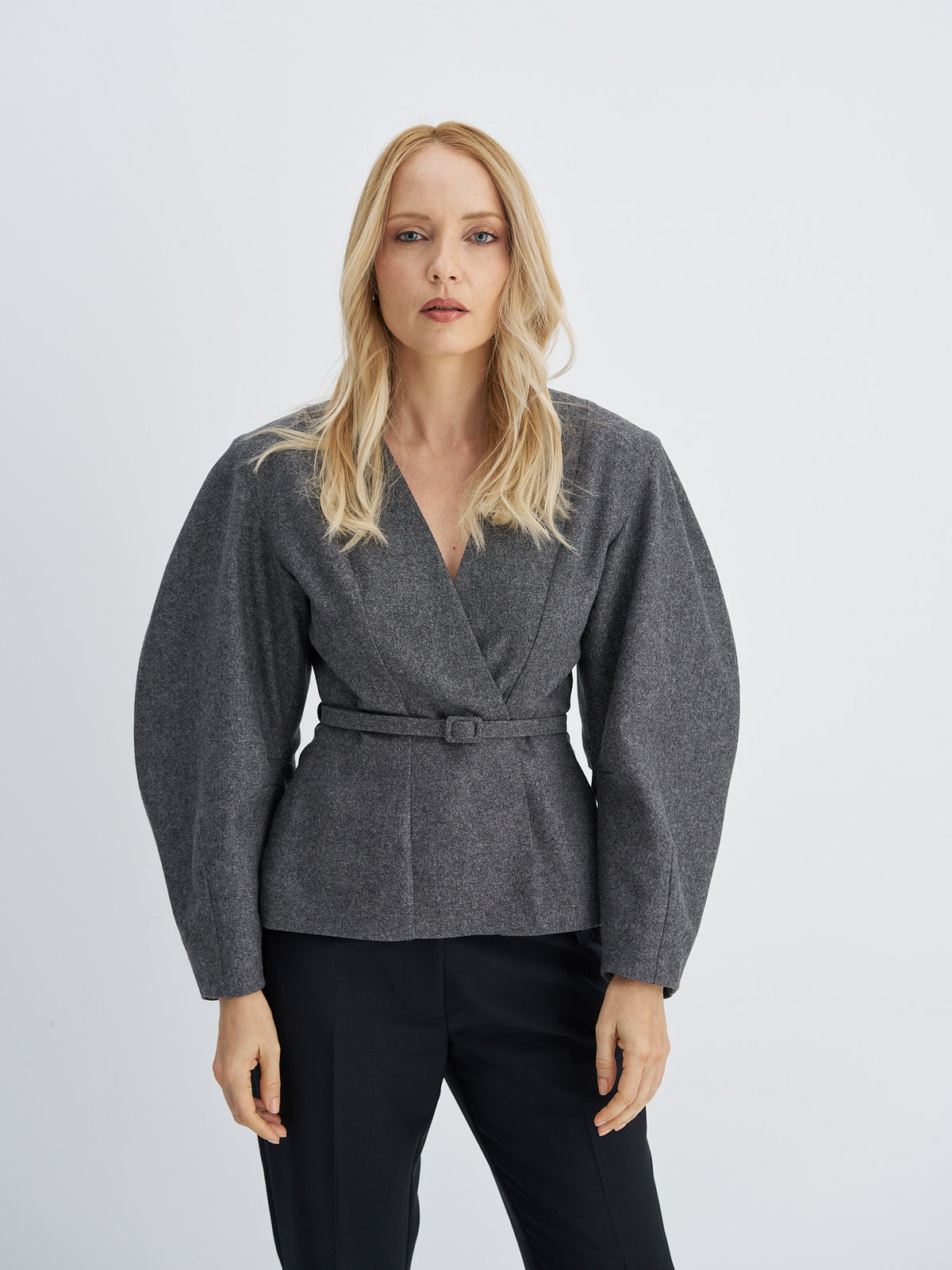 Front view of charcoal grey wool jacket with a V-neckline, sculptural sleeves and a matching narrow belt