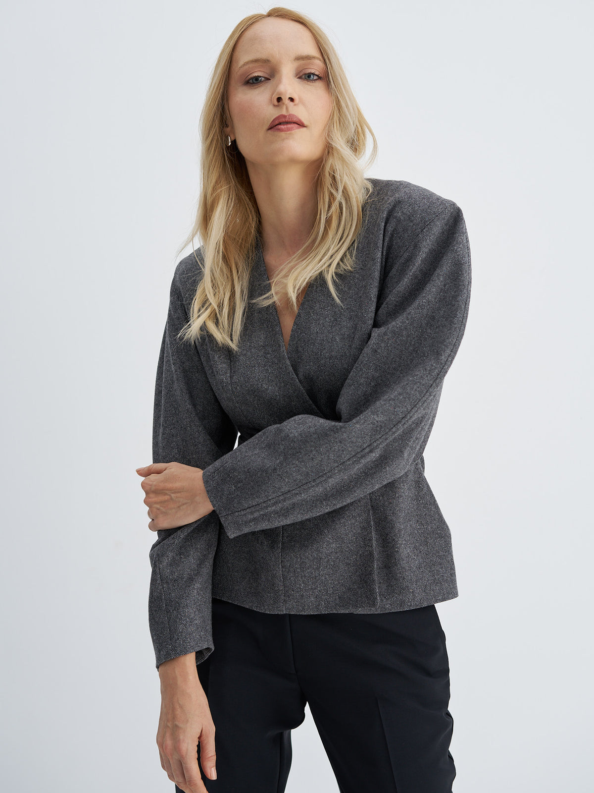 Charcoal grey wool jacket worn with arms crossed, showing shaped sleeves and a collarless V-neckline