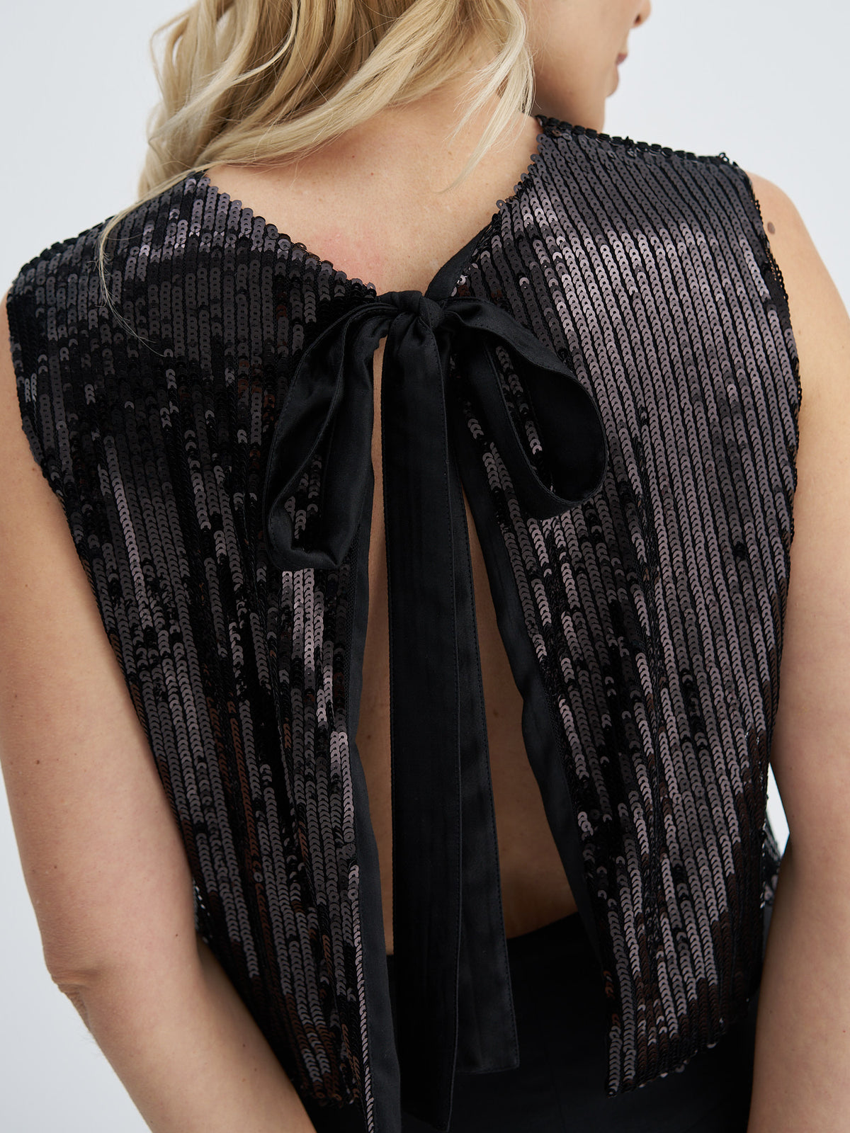 Close-up back view of a woman wearing a sleeveless black sequined vest with a tied back and open back design.