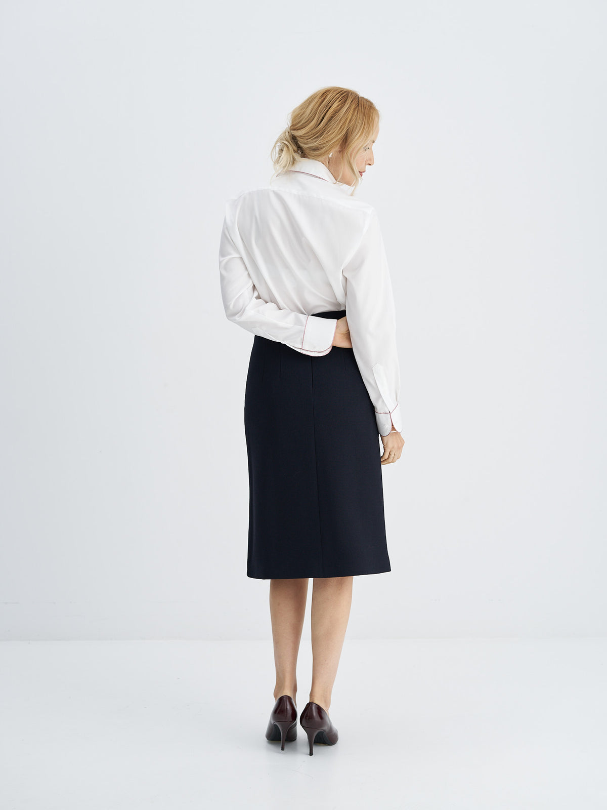 Three-quarter back view of white long-sleeved cotton shirt tucked into a dark midi skirt