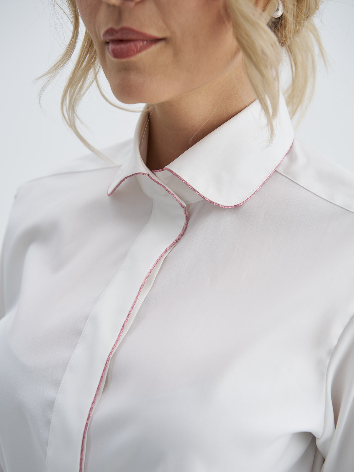 Close-up of white cotton shirt showing the rounded collar and front placket edged with pink metallic-thread piping