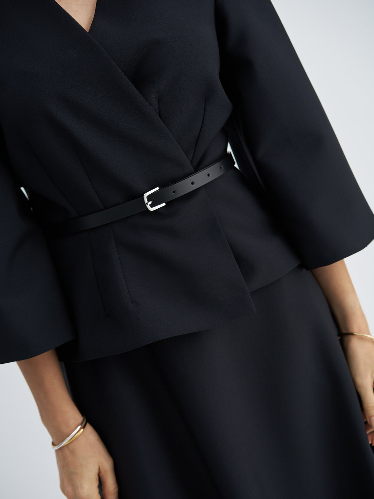 Close-up of the jacket’s overlapping front, waist darts and leather belt with a metal buckle