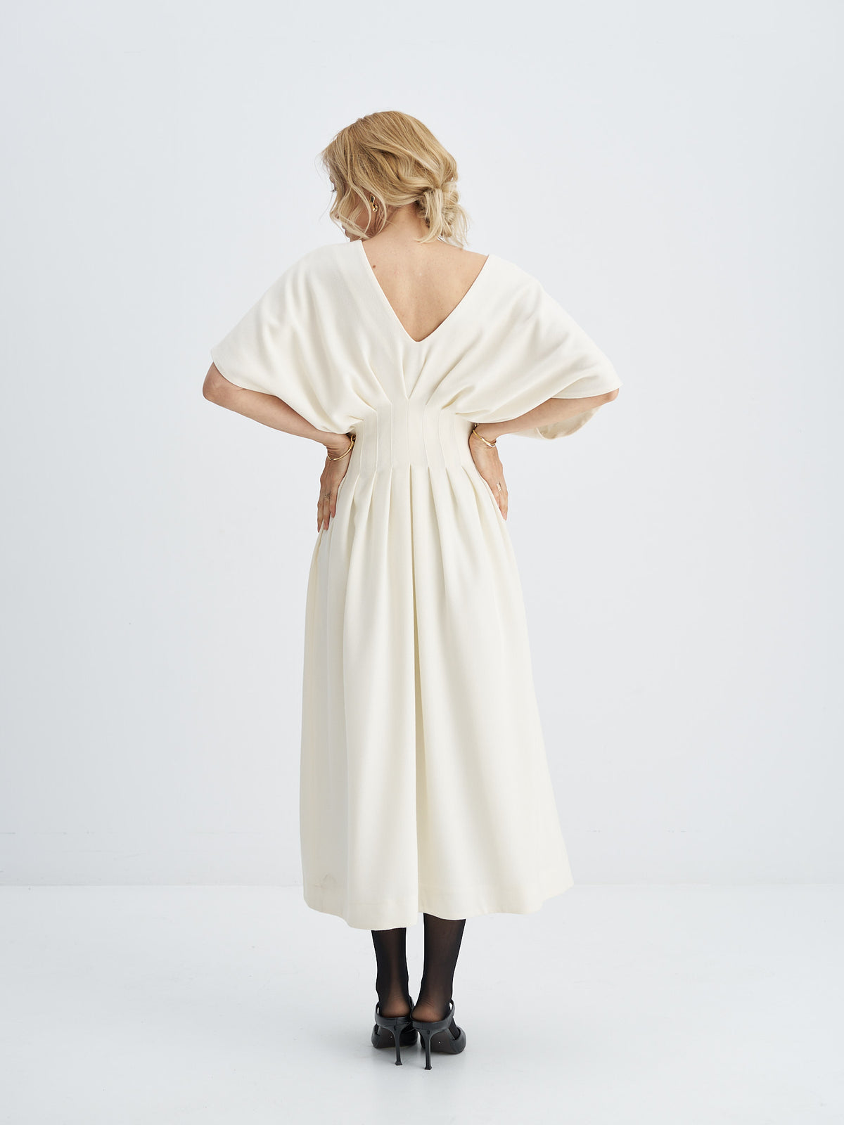 Back of ivory wool-crepe midi dress showing a V-shaped neckline, wide sleeves and pleats defining the waist