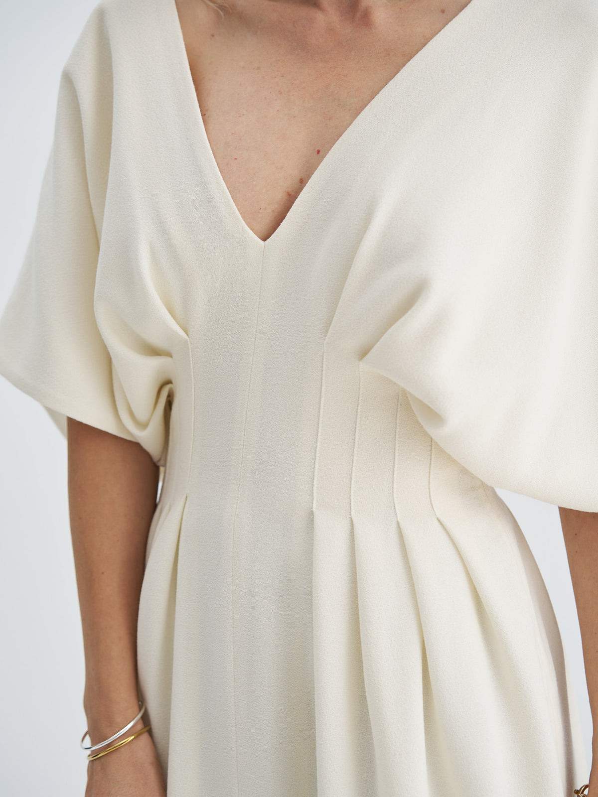 Close-up of ivory wool-crepe dress showing the fabric texture, V-neckline and stitched waist pleats