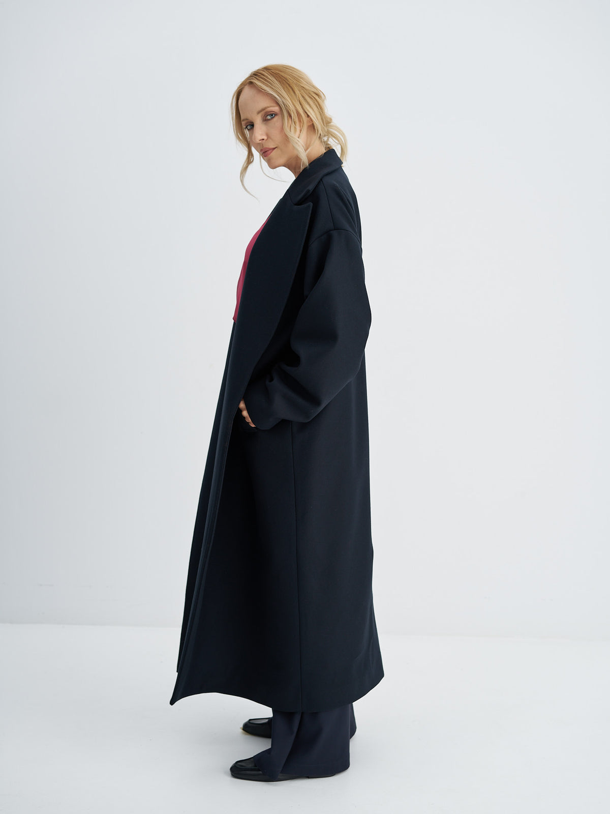 Side view of a long wool coat worn open, showing dropped shoulders and an oversized fit