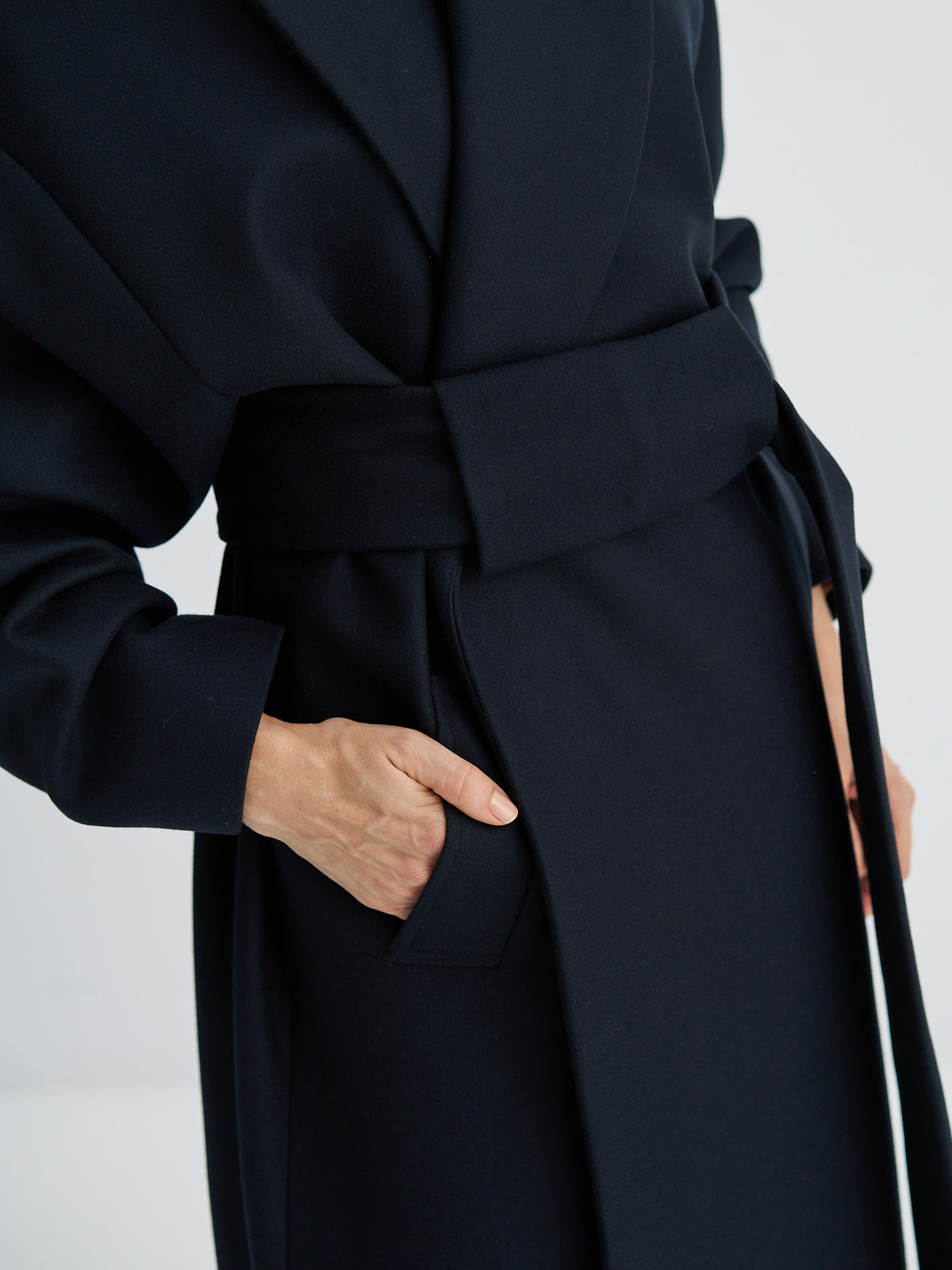Close-up of the wool coat’s wide belt panel, welt pocket and fabric texture