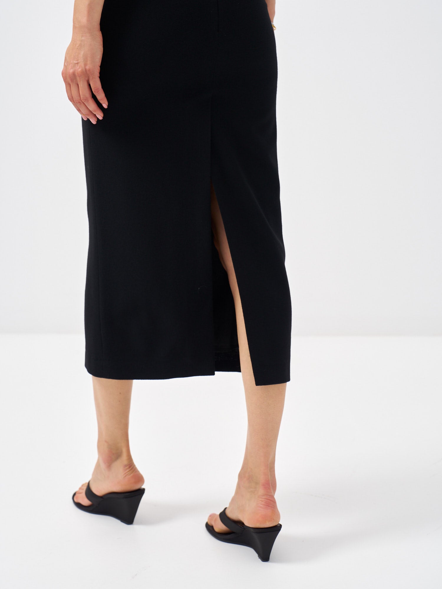 Back view of a black wool pencil skirt featuring a back slit and concealed zip closure